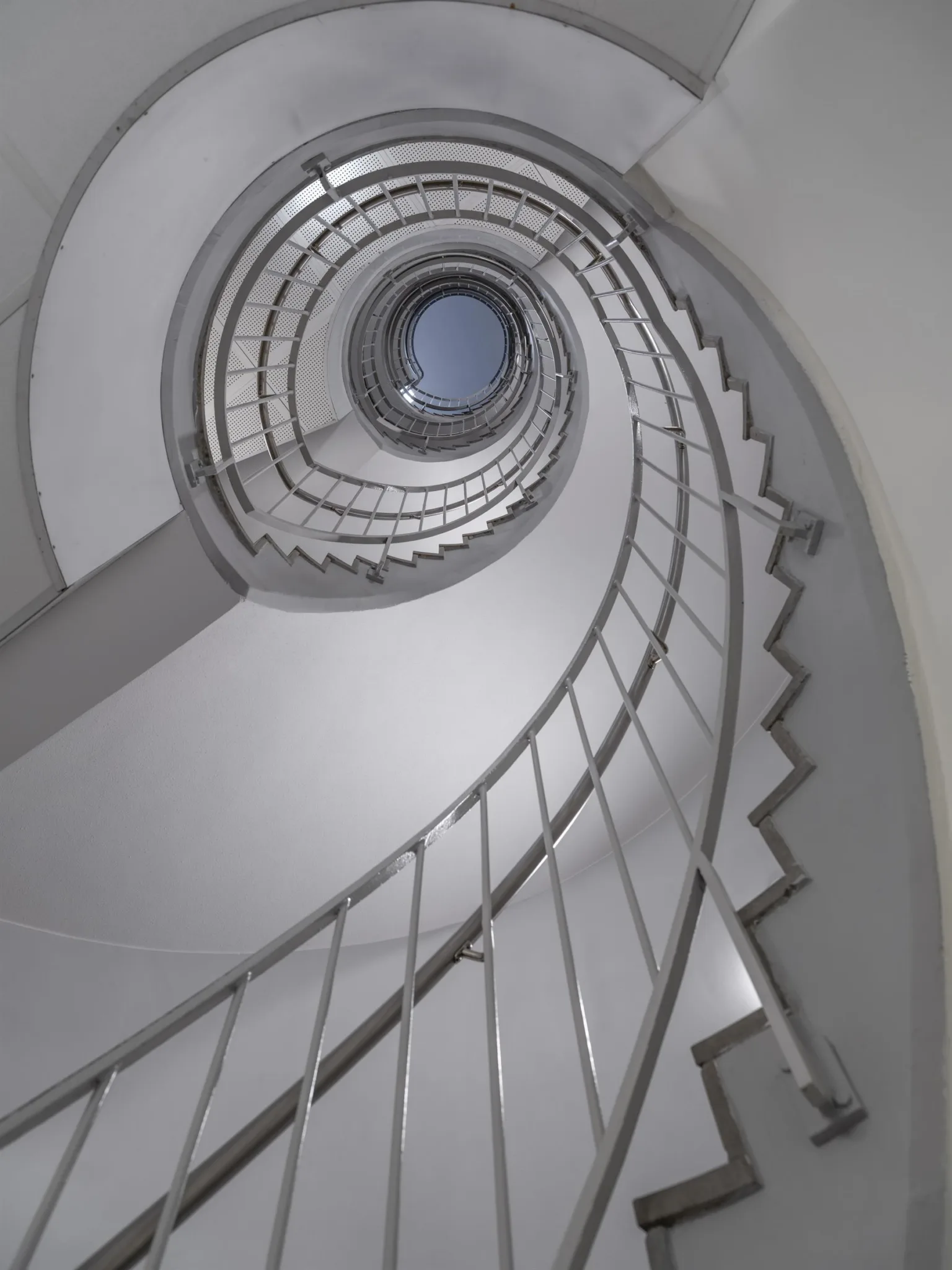 En spiralformad trappa fotograferad uppåt mot ett runt takfönster.