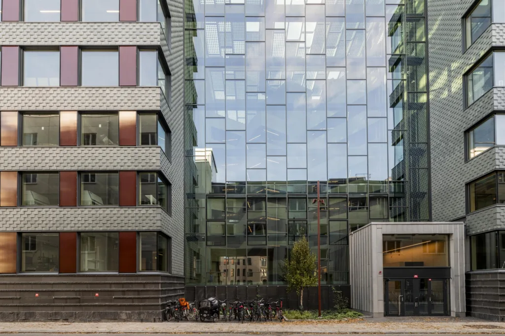 En modern byggnad med glasfasad, cyklar parkerade framför och reflektioner av himlen.