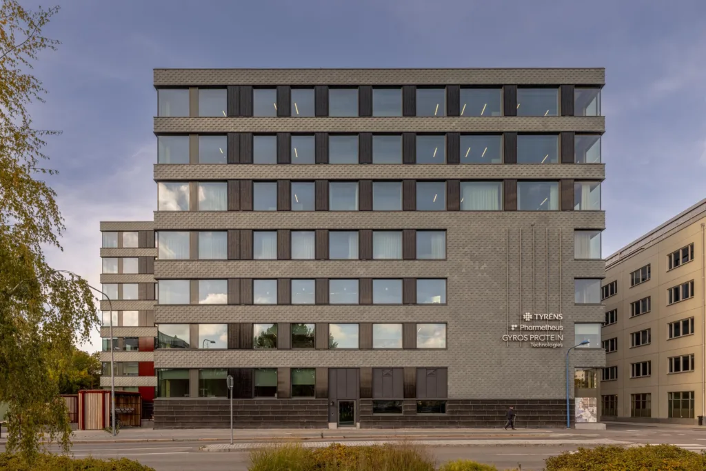 En grå kontorsbyggnad med många fönster och en skylt med text.