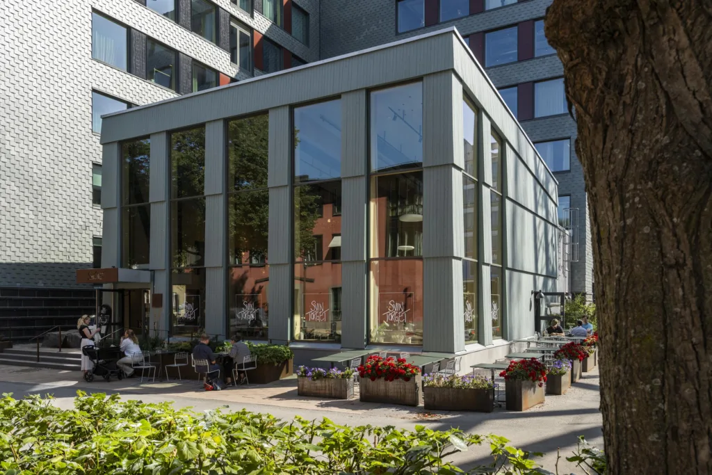 En modern byggnad med stora glasfönster, omgiven av grönska och blomsterdekorationer.