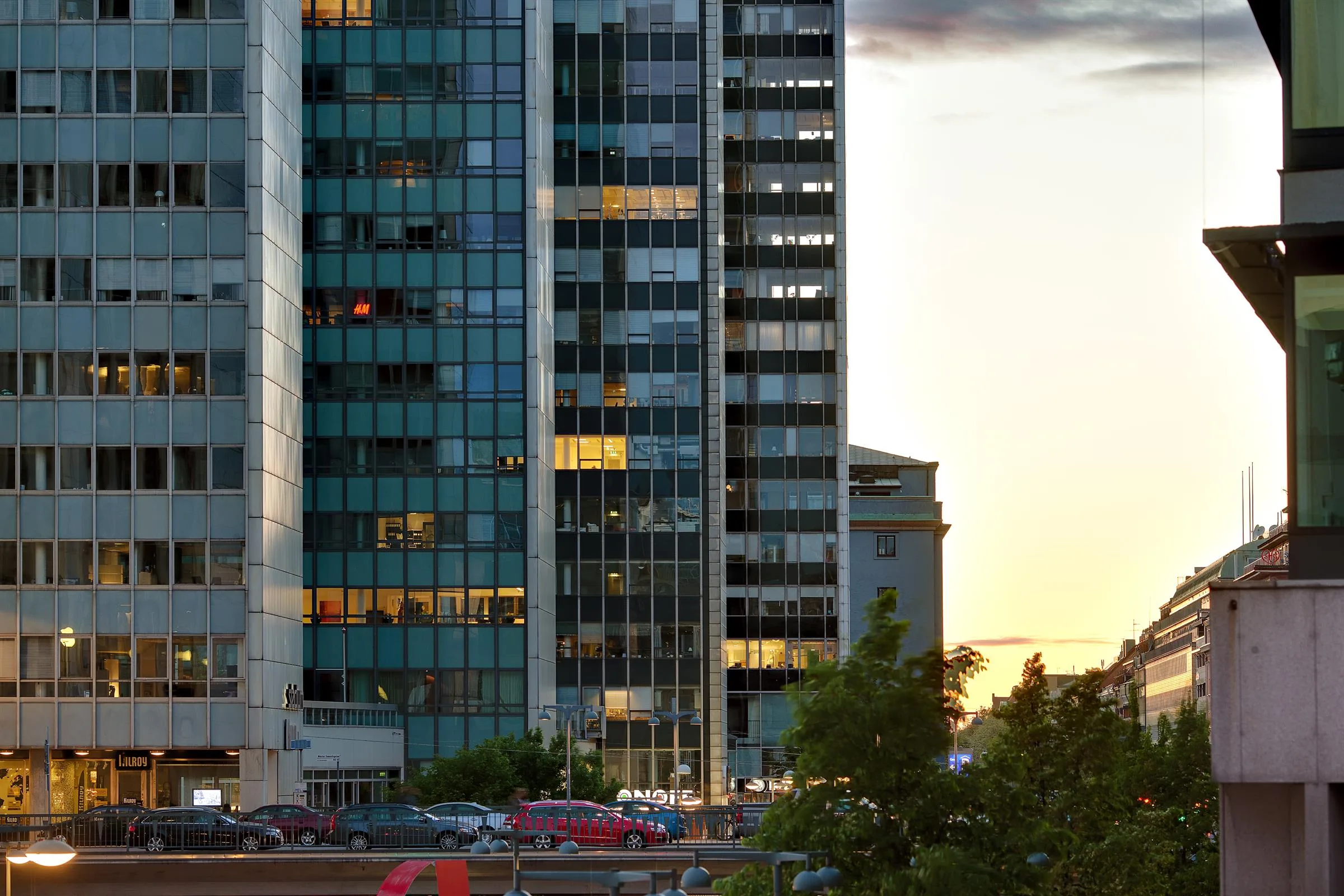 En hög byggnad med glasfasad reflekterar ljus vid solnedgång.