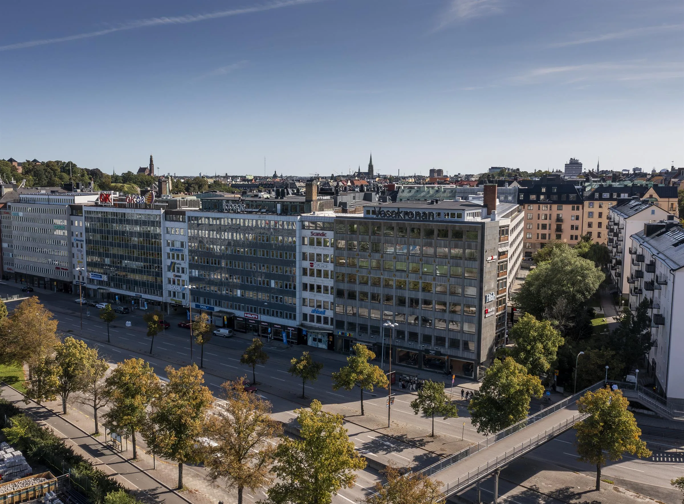 En lång byggnad med glasfönster, träd längs en bred gata under en klar himmel.