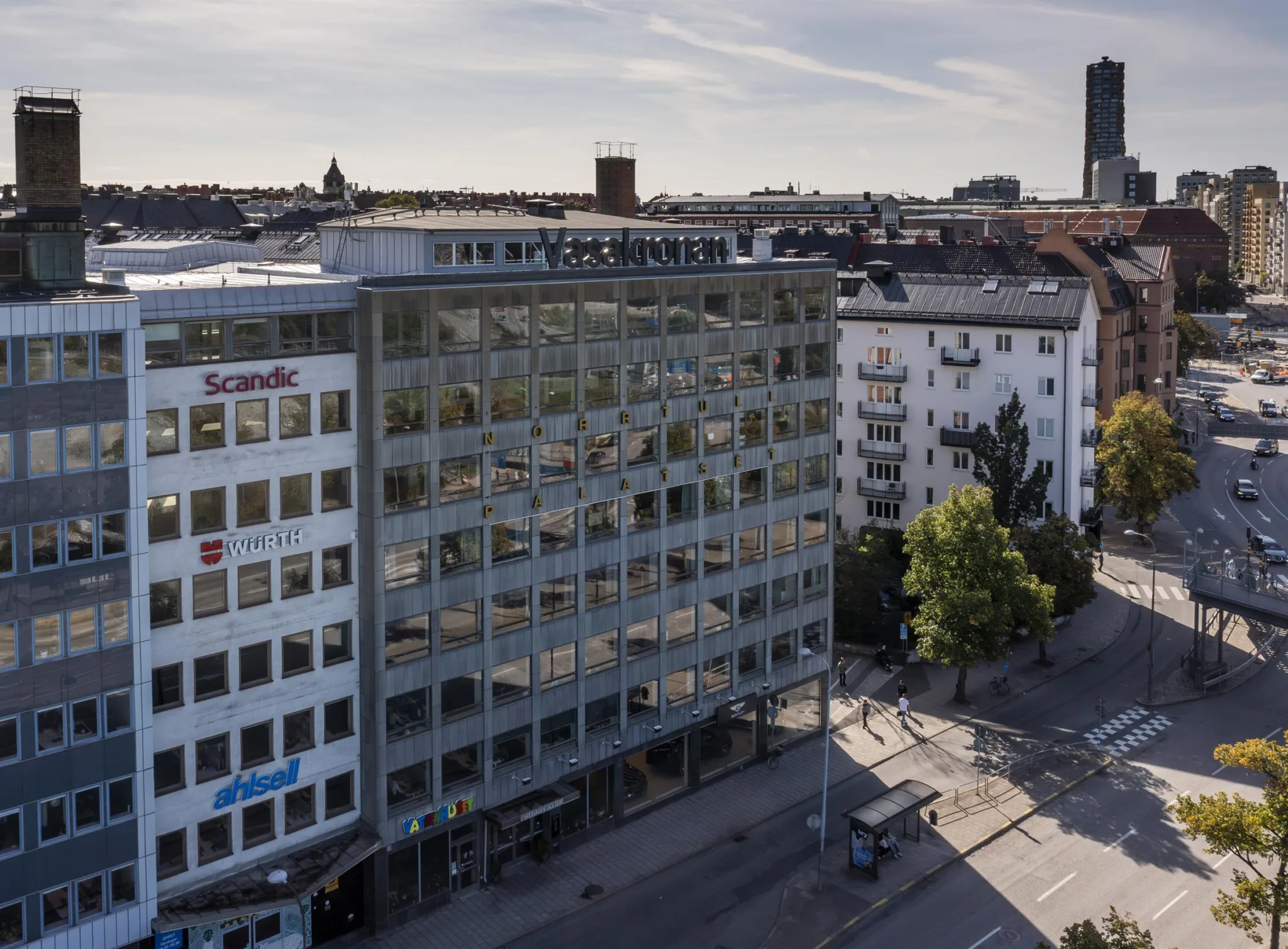 En vit byggnad med glasfönster och skyltar, omgiven av andra byggnader i stadsmiljö.