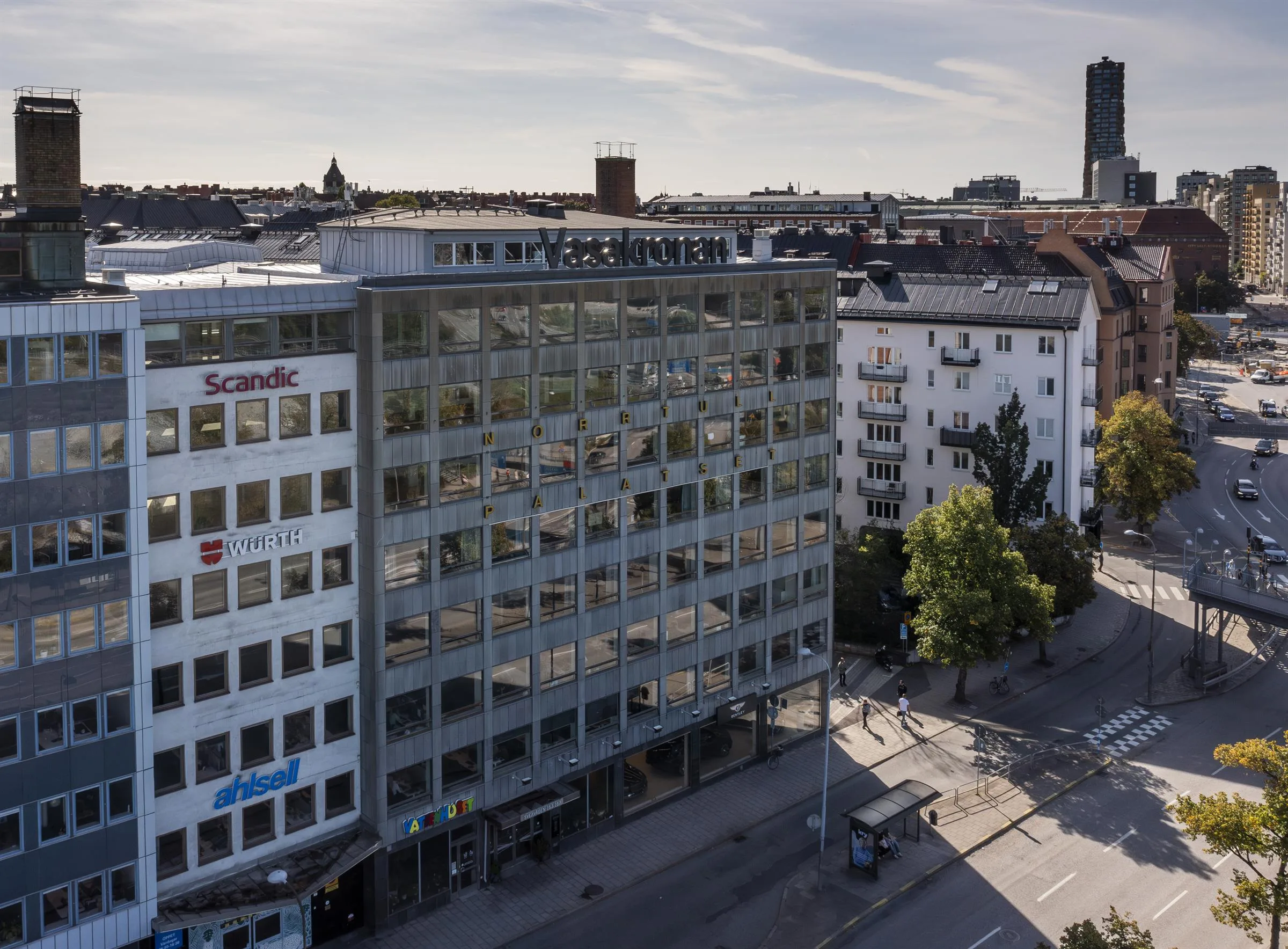 En vit byggnad med glasfönster och skyltar, omgiven av andra byggnader i stadsmiljö.