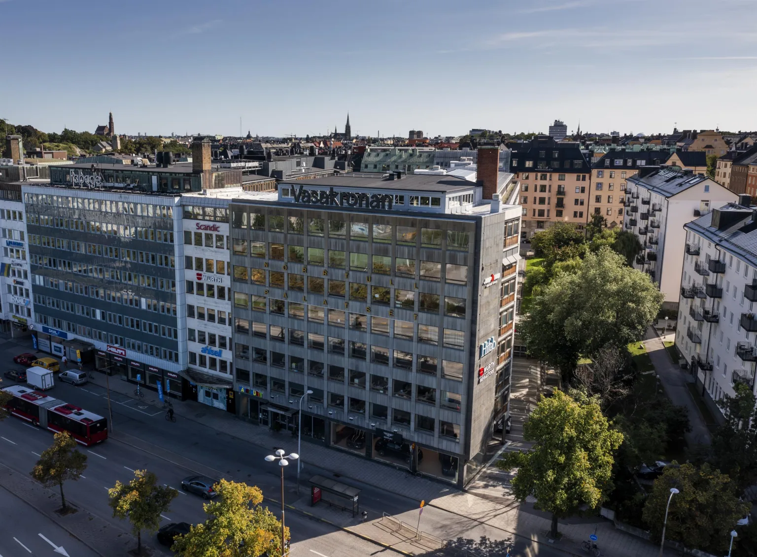 En byggnad med modern arkitektur, omgiven av grönska och stadsmiljö.