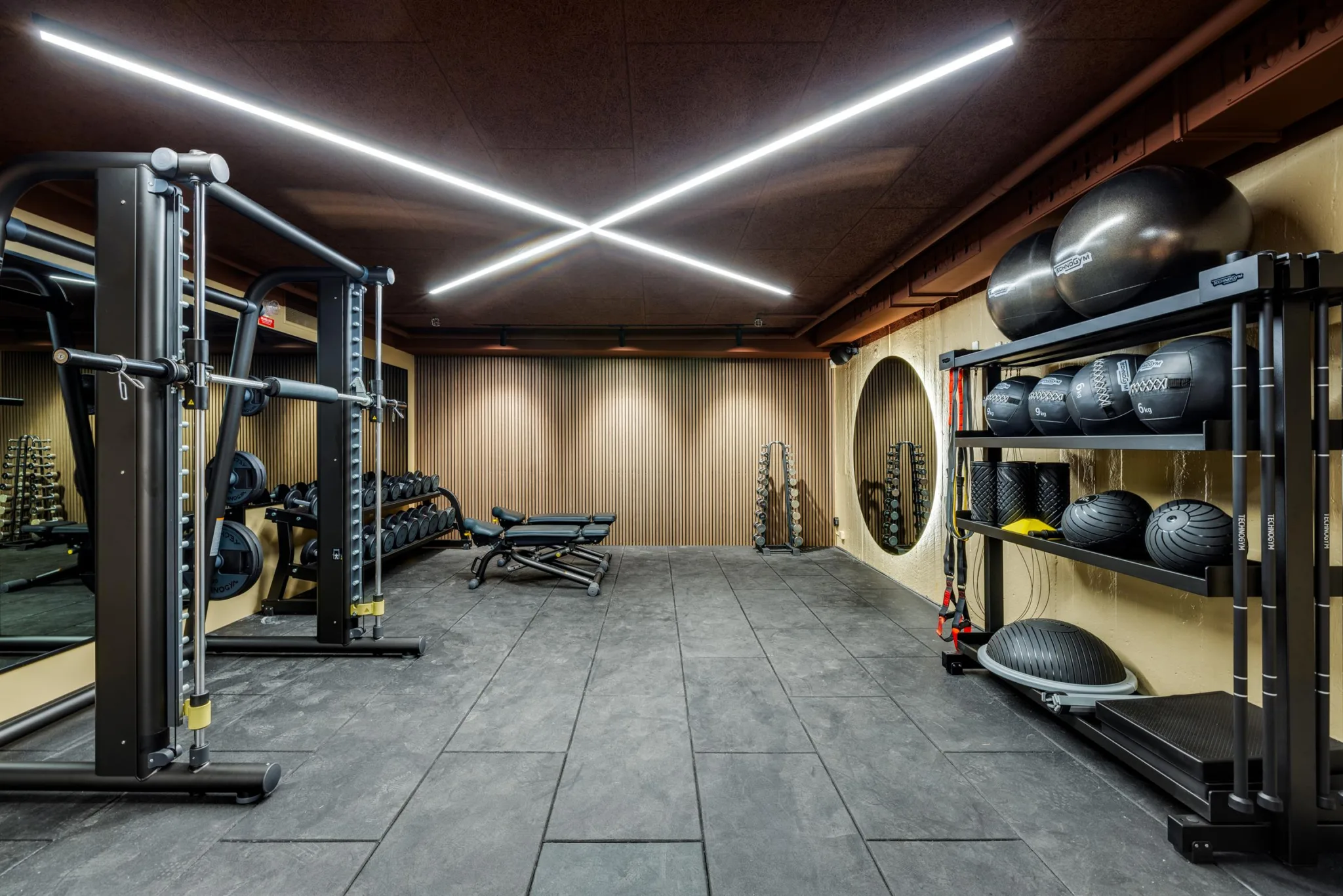 Ett gym med träningsutrustning, stora speglar och LED-belysning i taket.