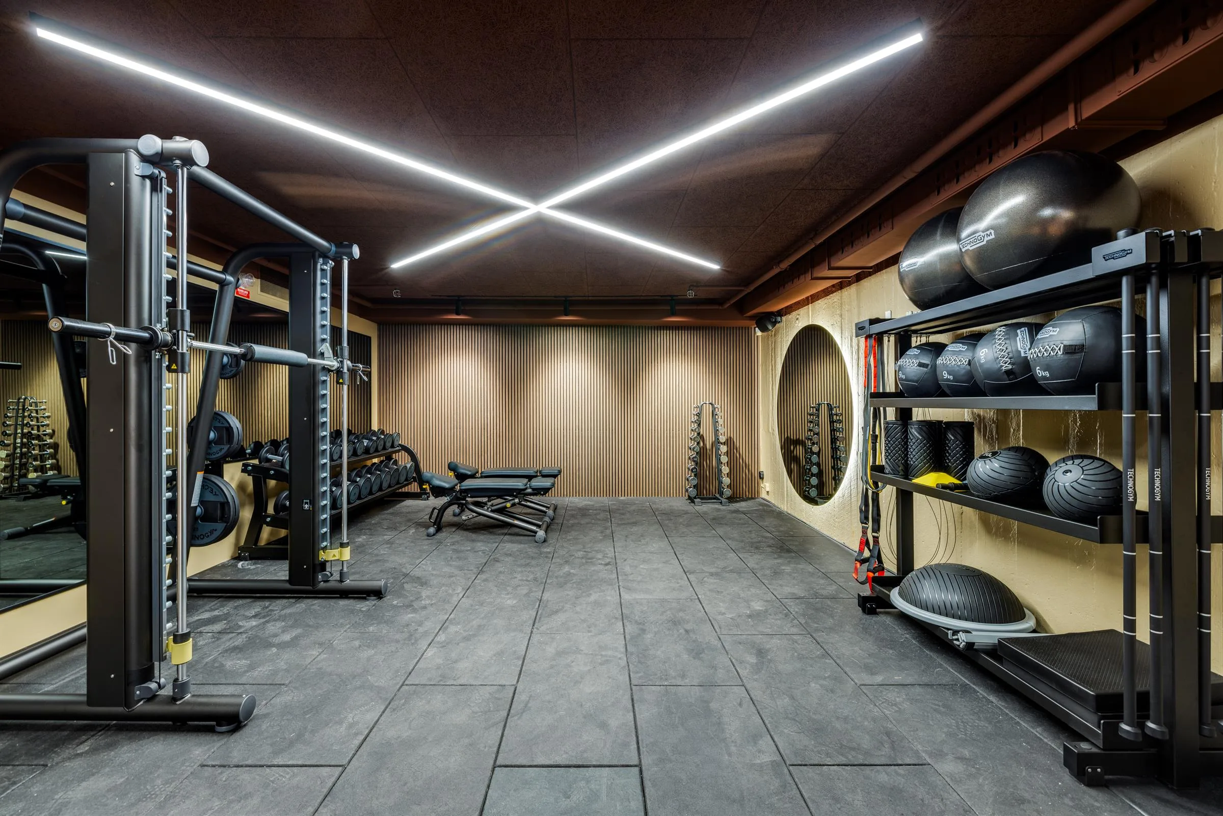 Ett gym med träningsutrustning, stora speglar och LED-belysning i taket.