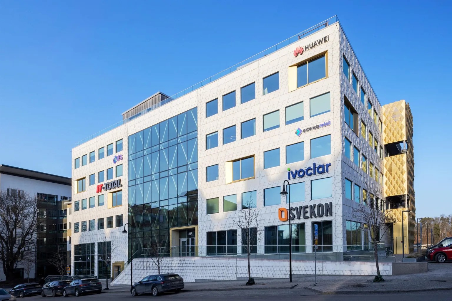 En modern kontorsbyggnad med vita fasader, glaspartier och skyltar med företagslogotyper.