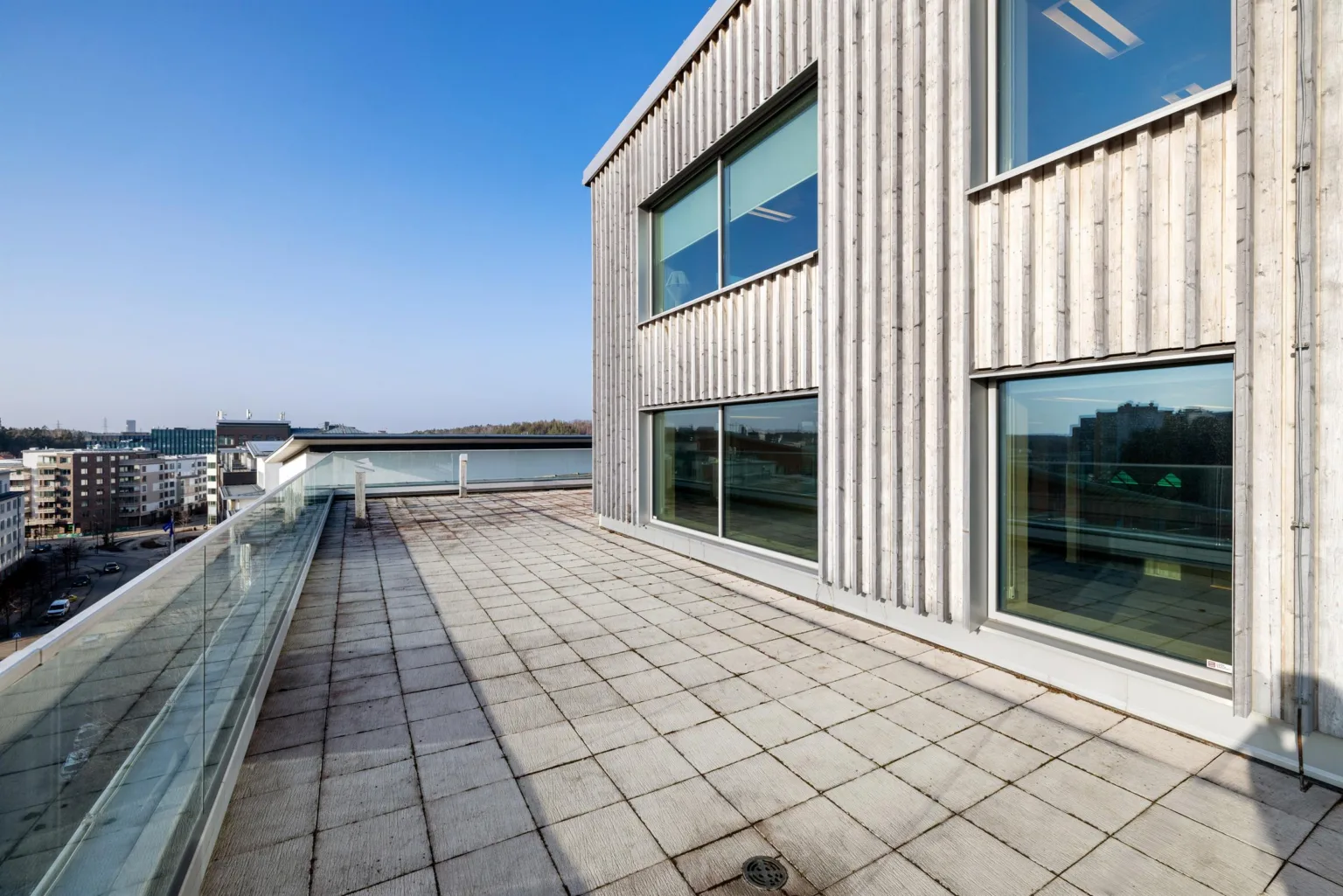 En stor terrass med plattor och ett modernt träklätt hus med stora fönster i bakgrunden.