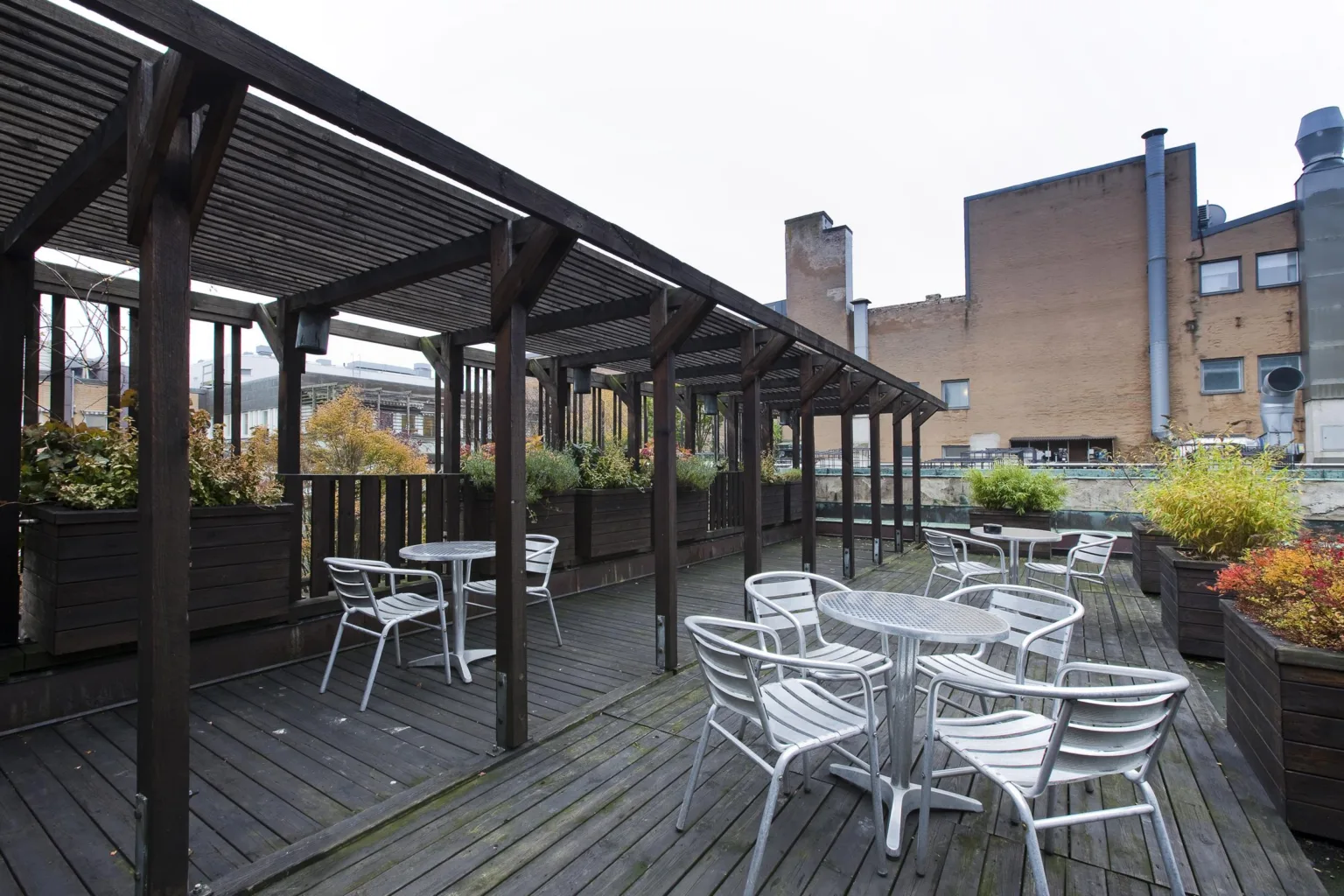 3. En utomhusterrass med trägolv, vita utemöbler och en pergola med växtlådor.