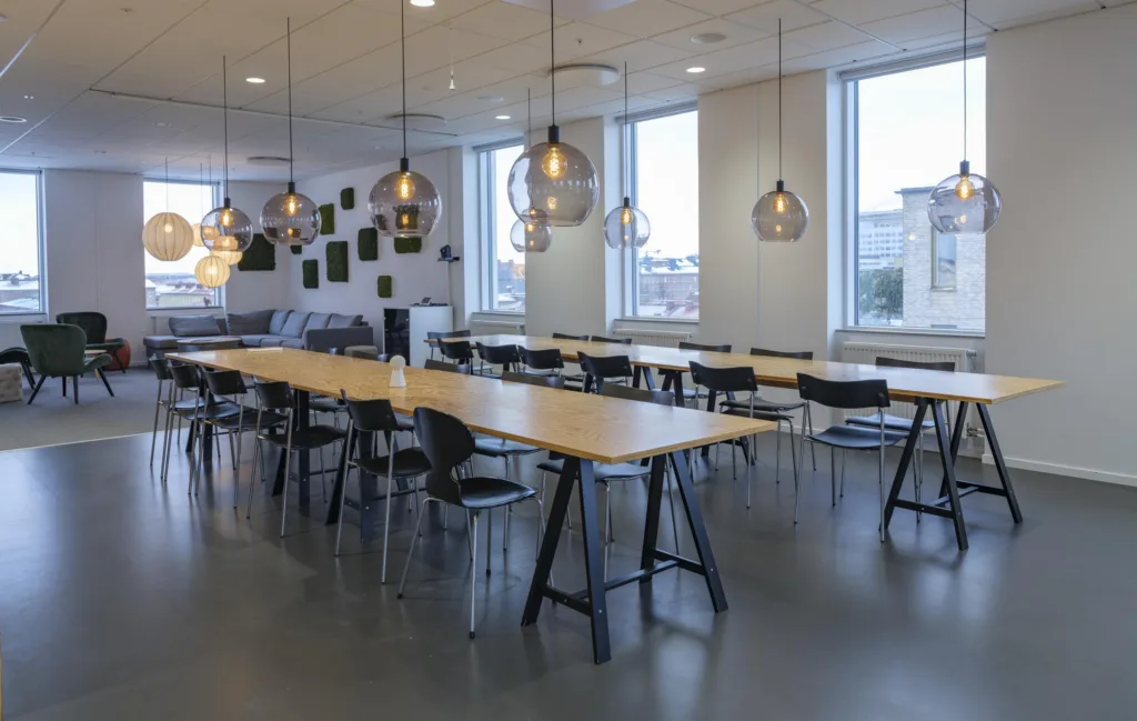 1. En matsal med långa bord, svarta stolar och moderna hängande lampor, omgiven av stora fönster.