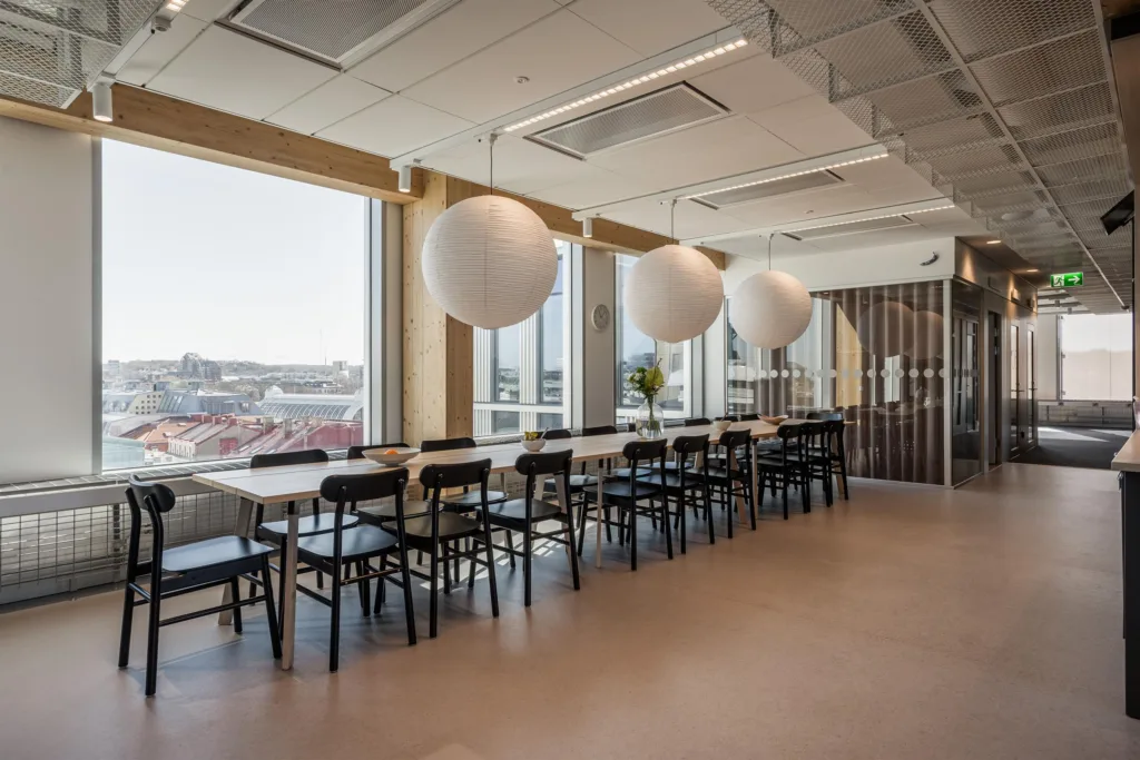 5. Ett ljust matsalsområde med långbord, svarta stolar och runda taklampor, samt stora fönster med utsikt.