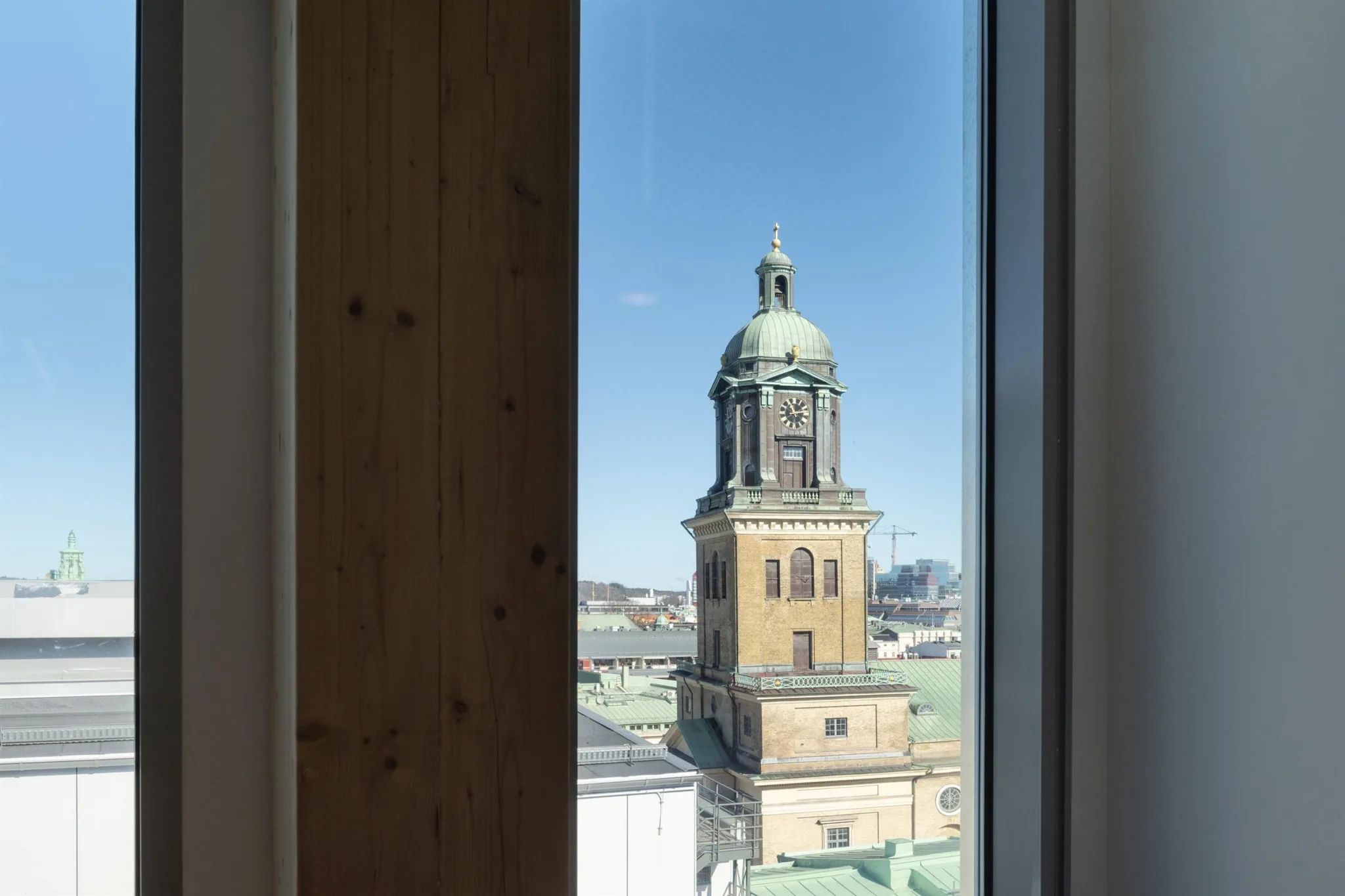 En kyrka med ett grönt kupoltak och klocktorn, sedd genom ett fönster med träram.