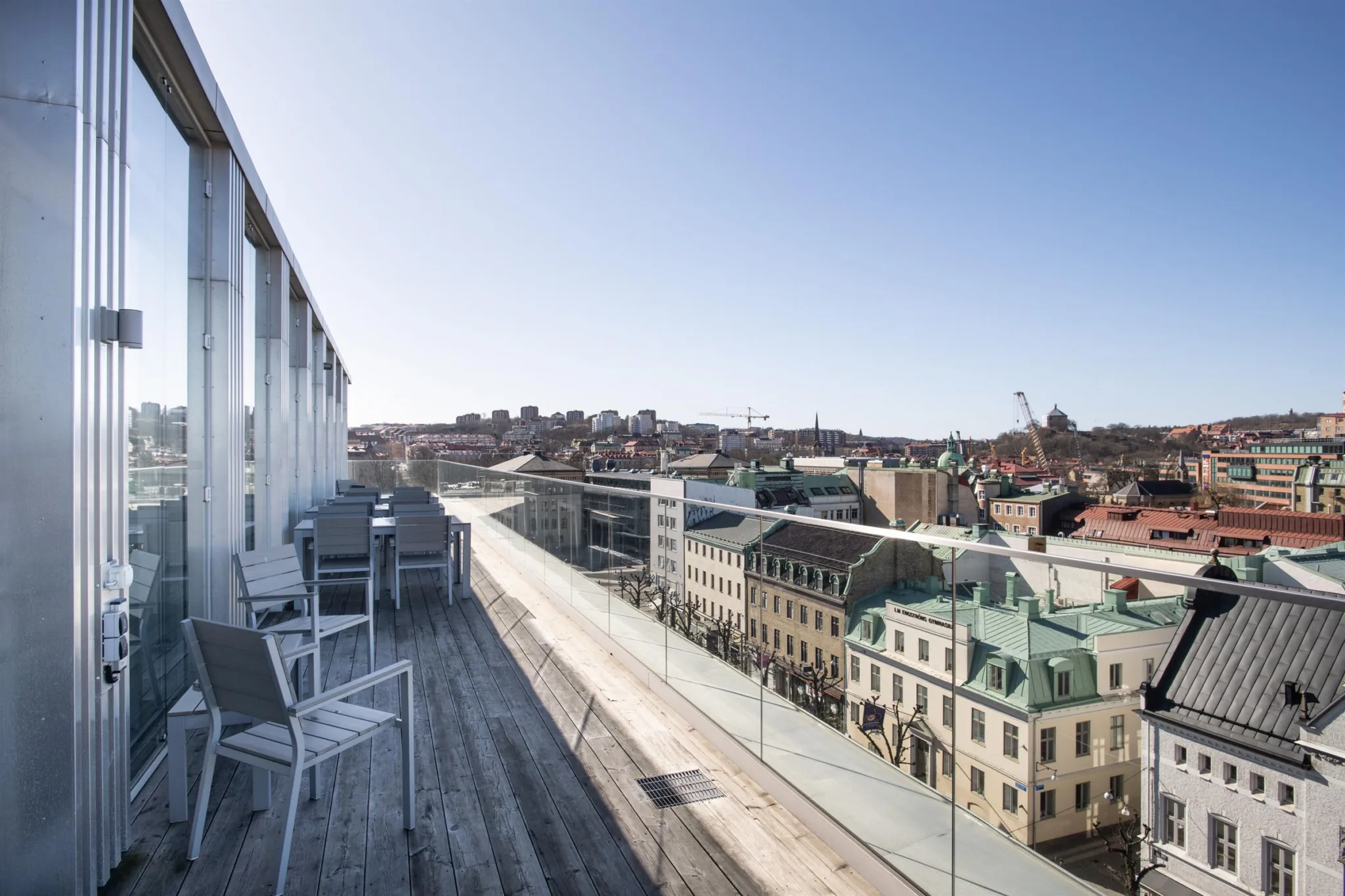 Takterrass med bord och stolar, med utsikt över en stadsmiljö och byggnader med klassisk arkitektur.