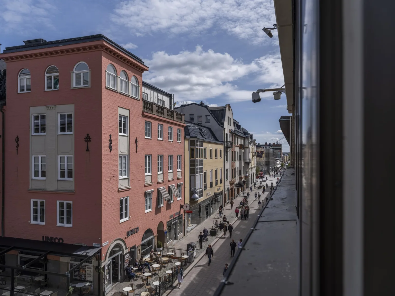 En gata med fotgängare, restauranger och färgglada byggnader under en delvis molnig himmel.