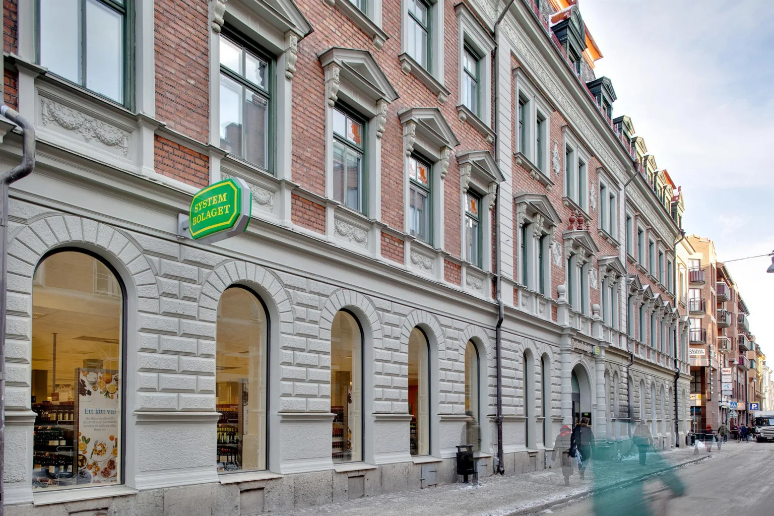 En tegelbyggnad med grönt skylt där det står "Akademibokhandeln"; gatan utanför är lugn med några förbipasserande.