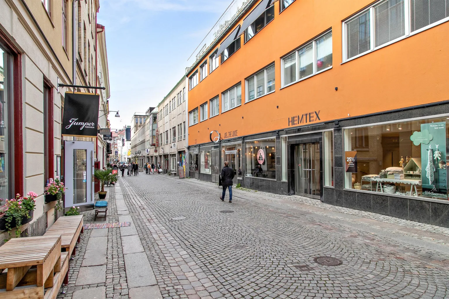 En gågata med kullersten där en orange byggnad med butiker syns till höger.