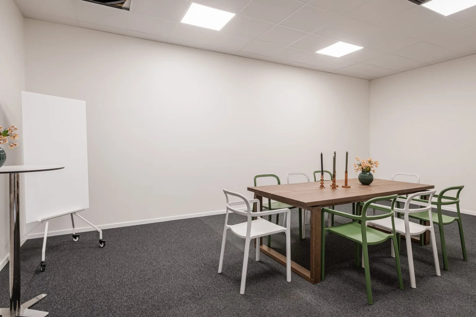 1. Ett mötesrum med ett träbord, stolar, en blädderblockstavla och minimalistisk inredning.