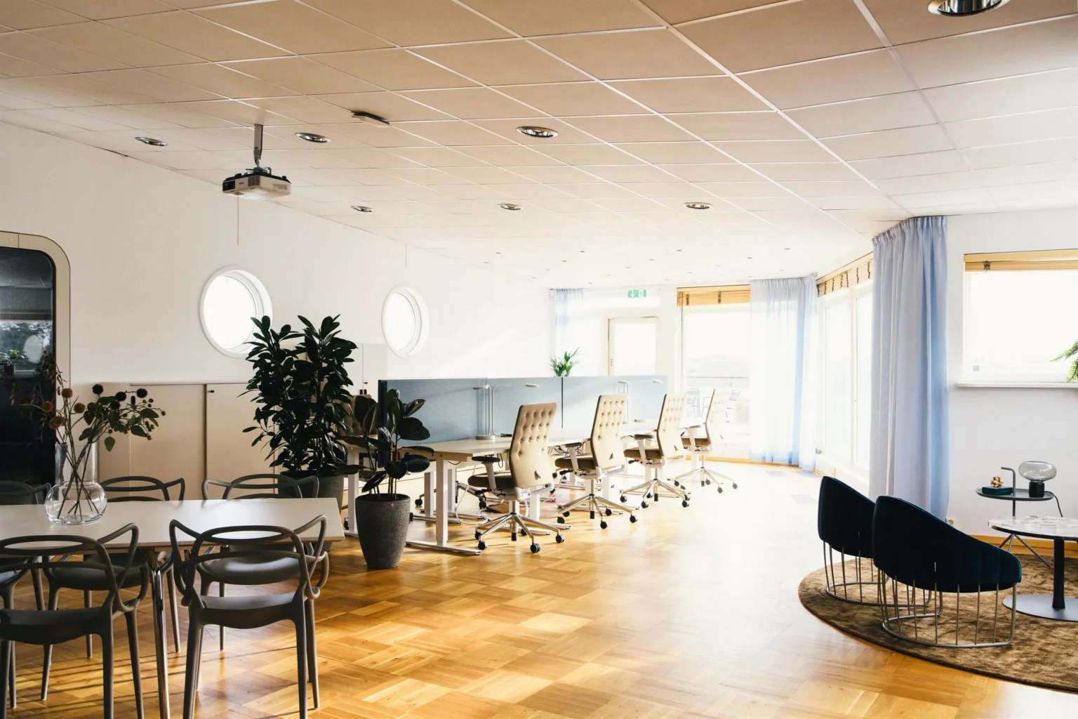 Ett öppet kontorsutrymme med skrivbord, stolar, växter och stora fönster.
