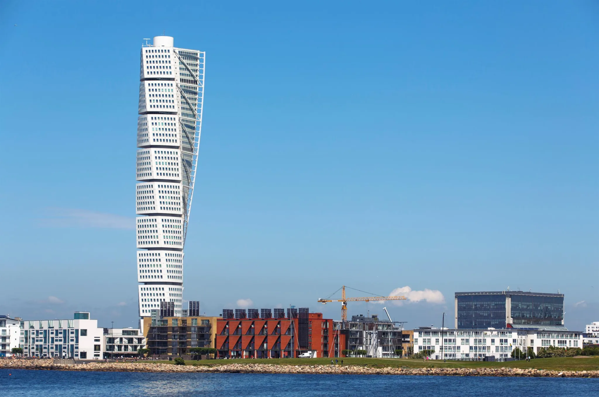 Turning Torso-skyskrapa i Malmö mot en blå himmel, omgiven av byggnader vid vattnet.