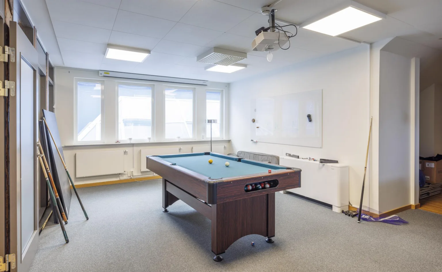 Ett rum med ett biljardbord, projektor och stora fönster.