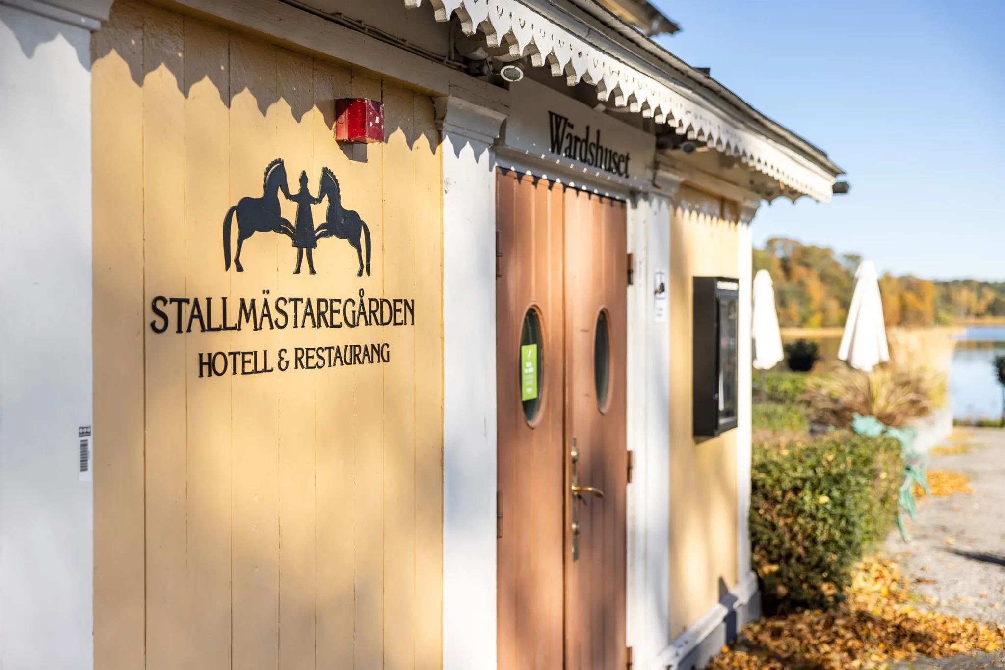 Entré till byggnaden Tallmästaregården Hotell & Restaurang, med en träfasad, logotyp och en dörr.