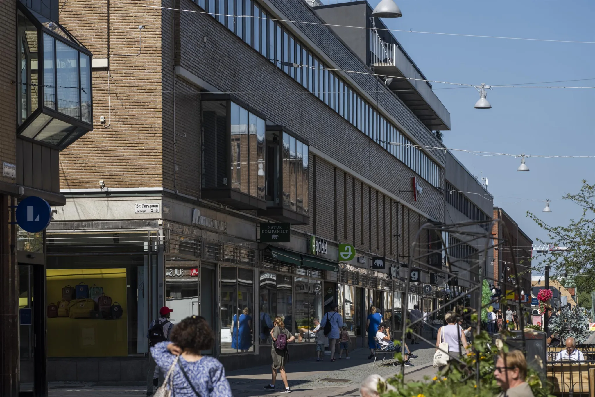 En stadsmiljö med människor som promenerar längs en gata, omgiven av byggnader och affärer.