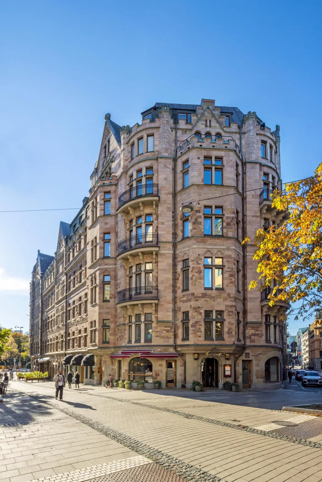 4. En hörnbyggnad med stenfasad, balkonger och många fönster, en solig dag med träd i förgrunden.