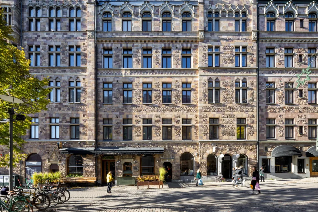 2. En stor stenfasad med många fönster, människor och cyklar på gatan framför byggnaden.