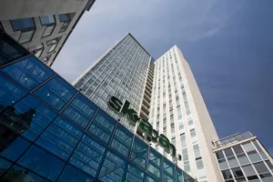 En hög byggnad med glasfasad och texten "Skanska" synlig på framsidan, mot en blå himmel.