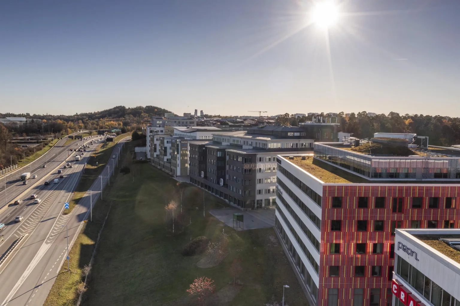 3. En vy över flera kontorsbyggnader i ett campusområde, med solen som lyser starkt i bakgrunden.