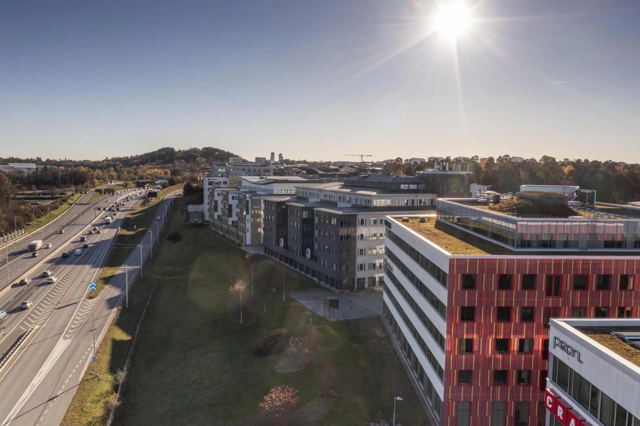 3. En vy över flera kontorsbyggnader i ett campusområde, med solen som lyser starkt i bakgrunden.