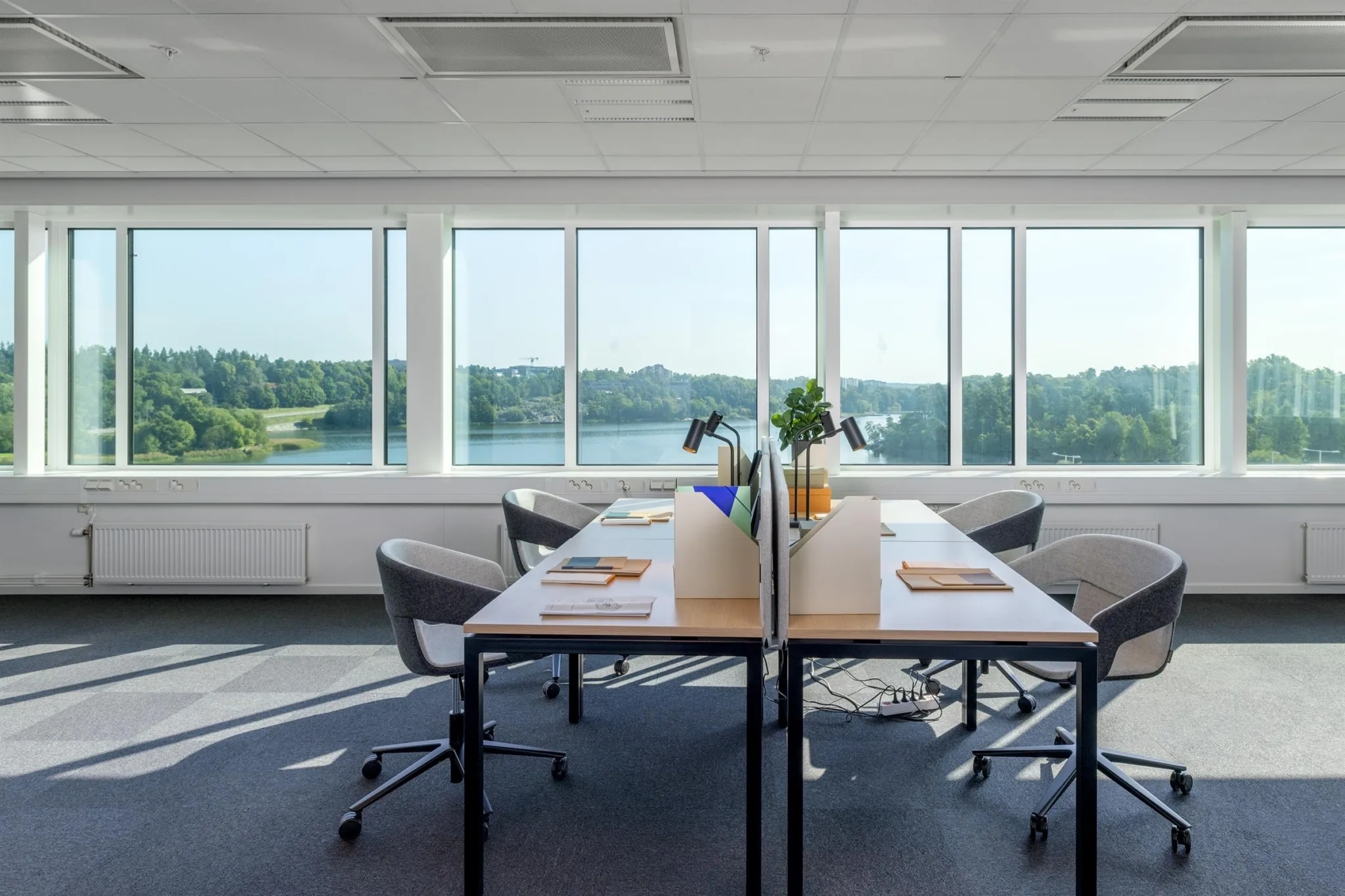 2. Ett ljust kontor med stora fönster, två skrivbord och utsikt över en sjö.