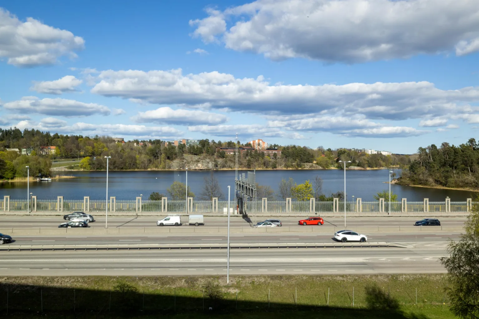 1. En motorväg med flera bilar och en sjö samt träd i bakgrunden under en blå himmel med moln.