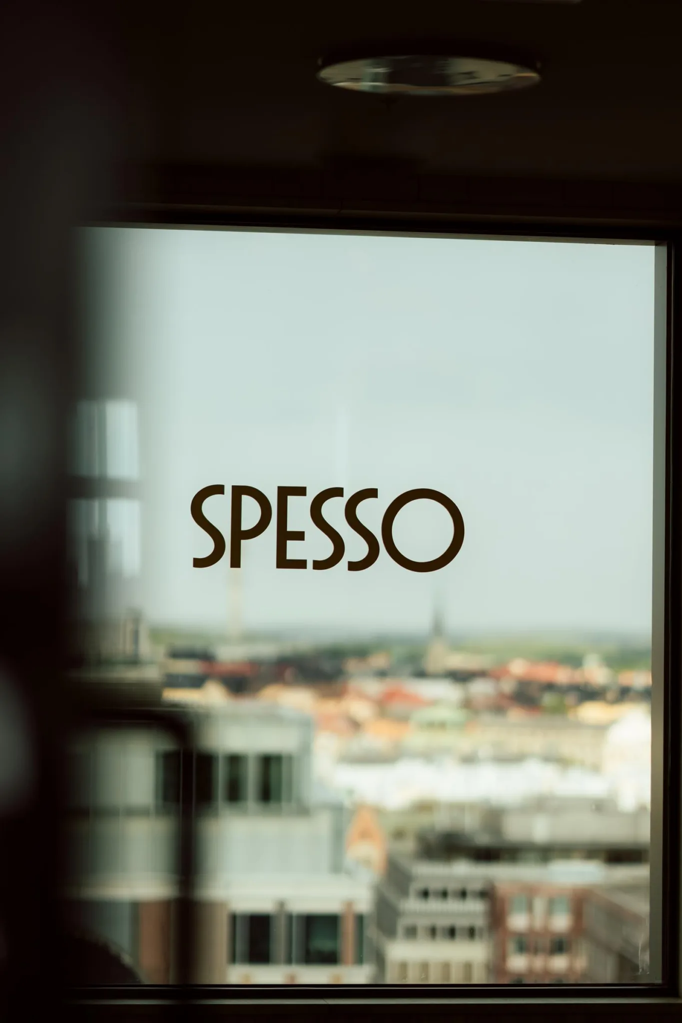 Texten "SPESSO" syns på glas med en stadsutsikt i bakgrunden.