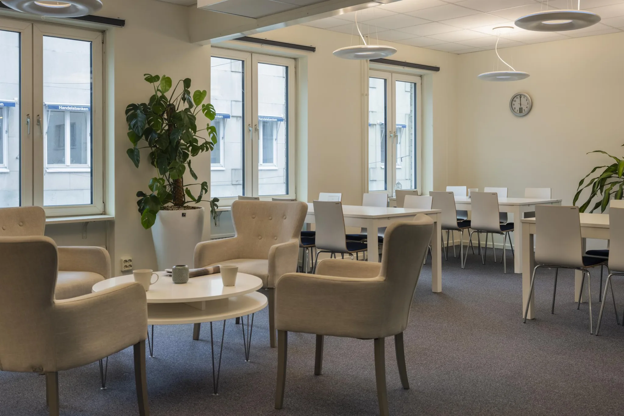 3. En lounge med fåtöljer, små bord och en grön växt vid fönstret.