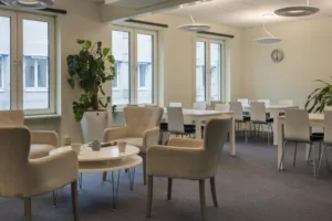 3. En lounge med fåtöljer, små bord och en grön växt vid fönstret.