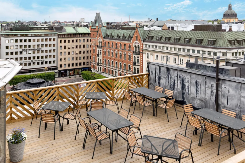 En takterrass med flera bord och stolar; utsikt över omkringliggande byggnader.