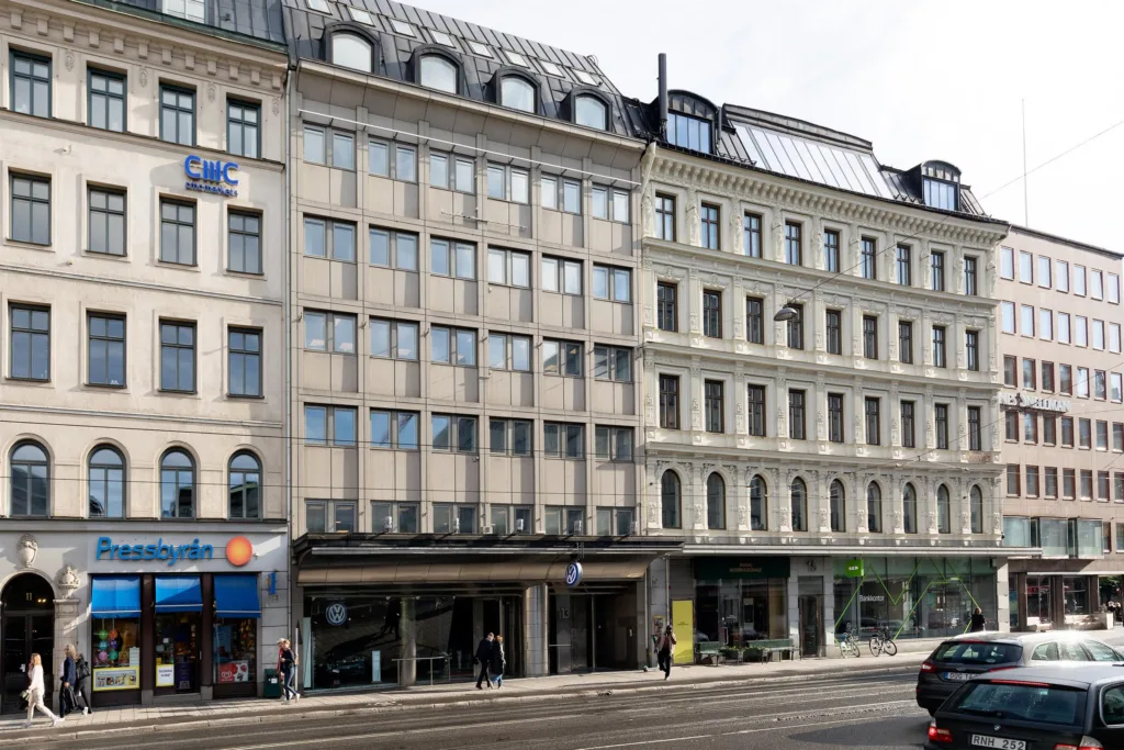 En rad byggnader med varierande fasader längs en stadsgata med trottoar och butiksskyltar.