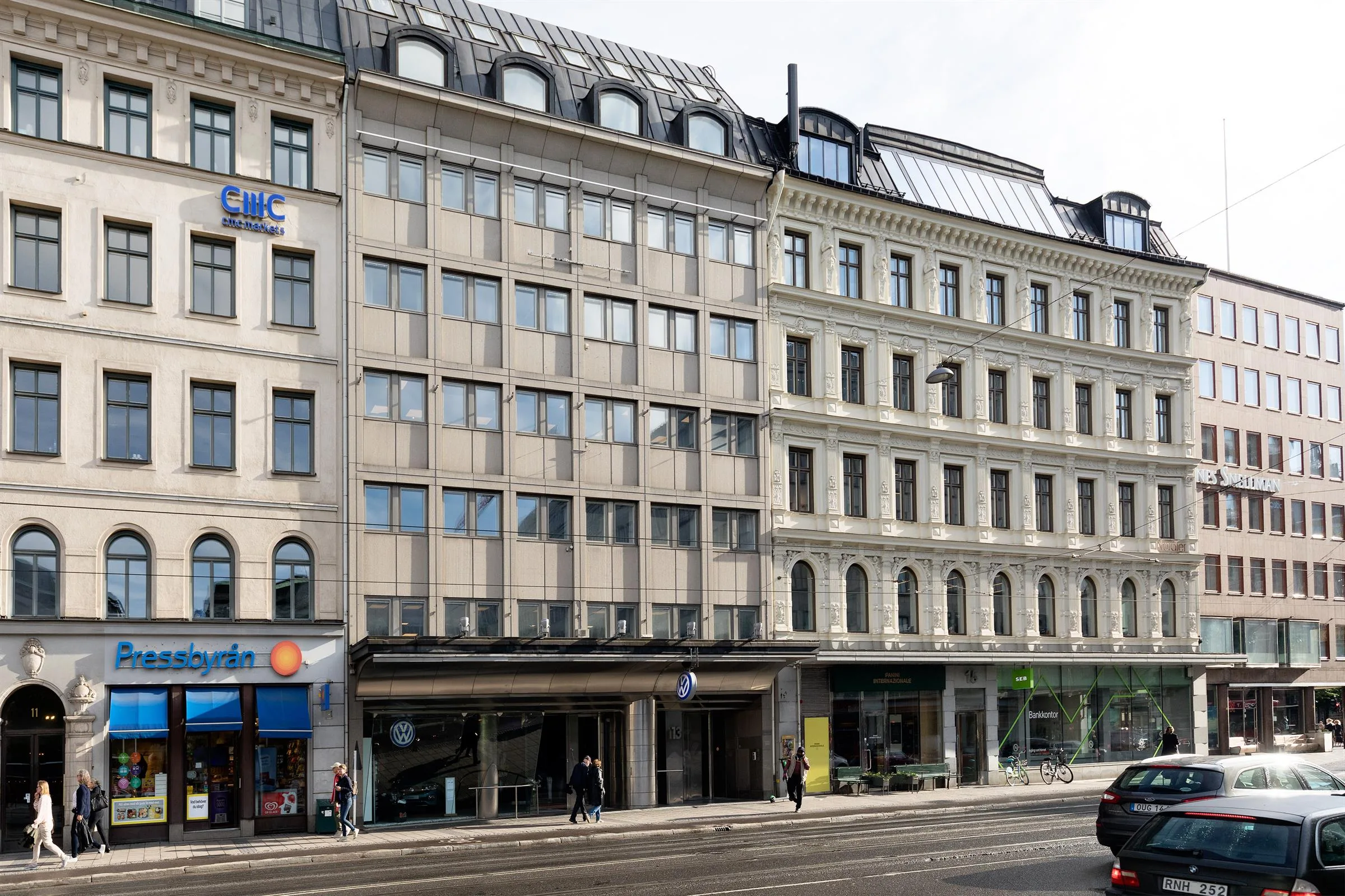 En rad byggnader med varierande fasader längs en stadsgata med trottoar och butiksskyltar.