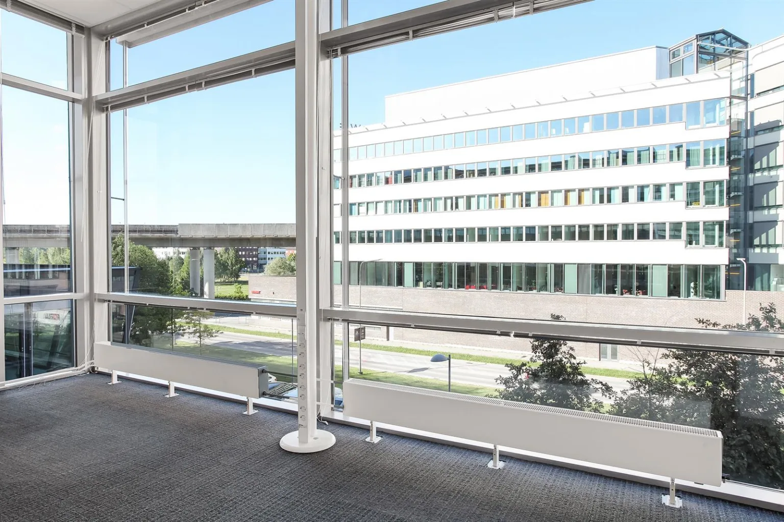 3. Utsikt från ett kontor med stora fönster mot en modern byggnad och grönska.