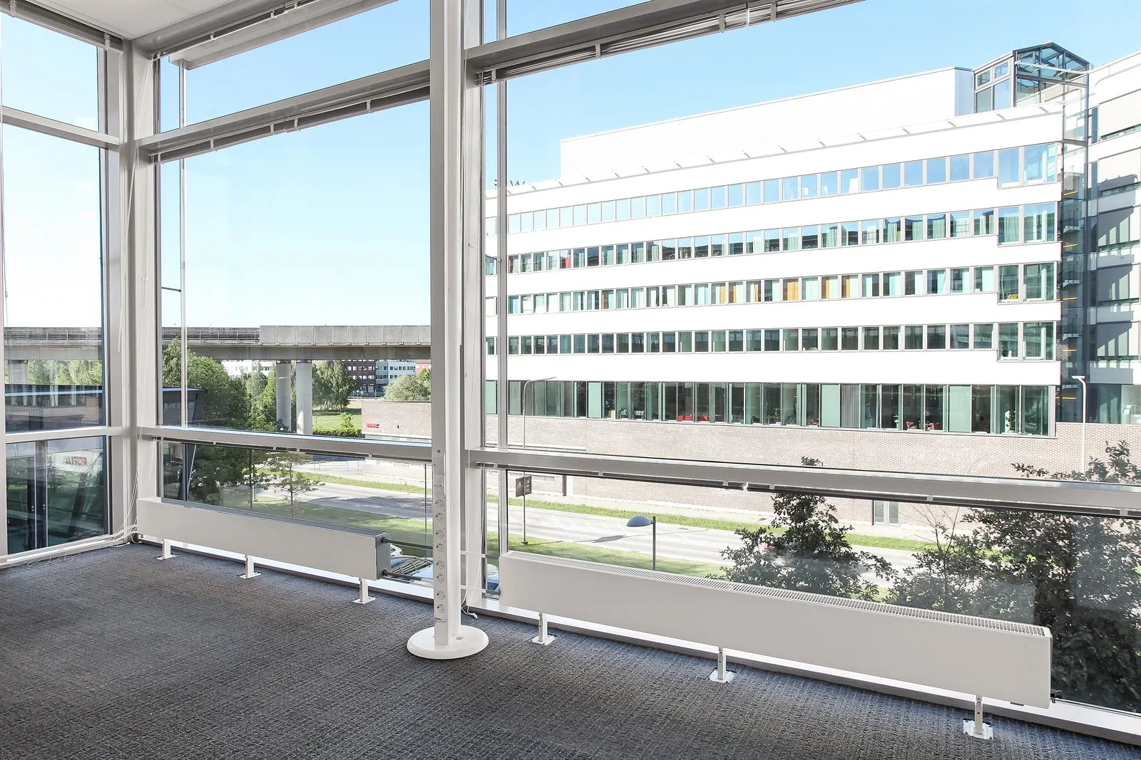 3. Utsikt från ett kontor med stora fönster mot en modern byggnad och grönska.