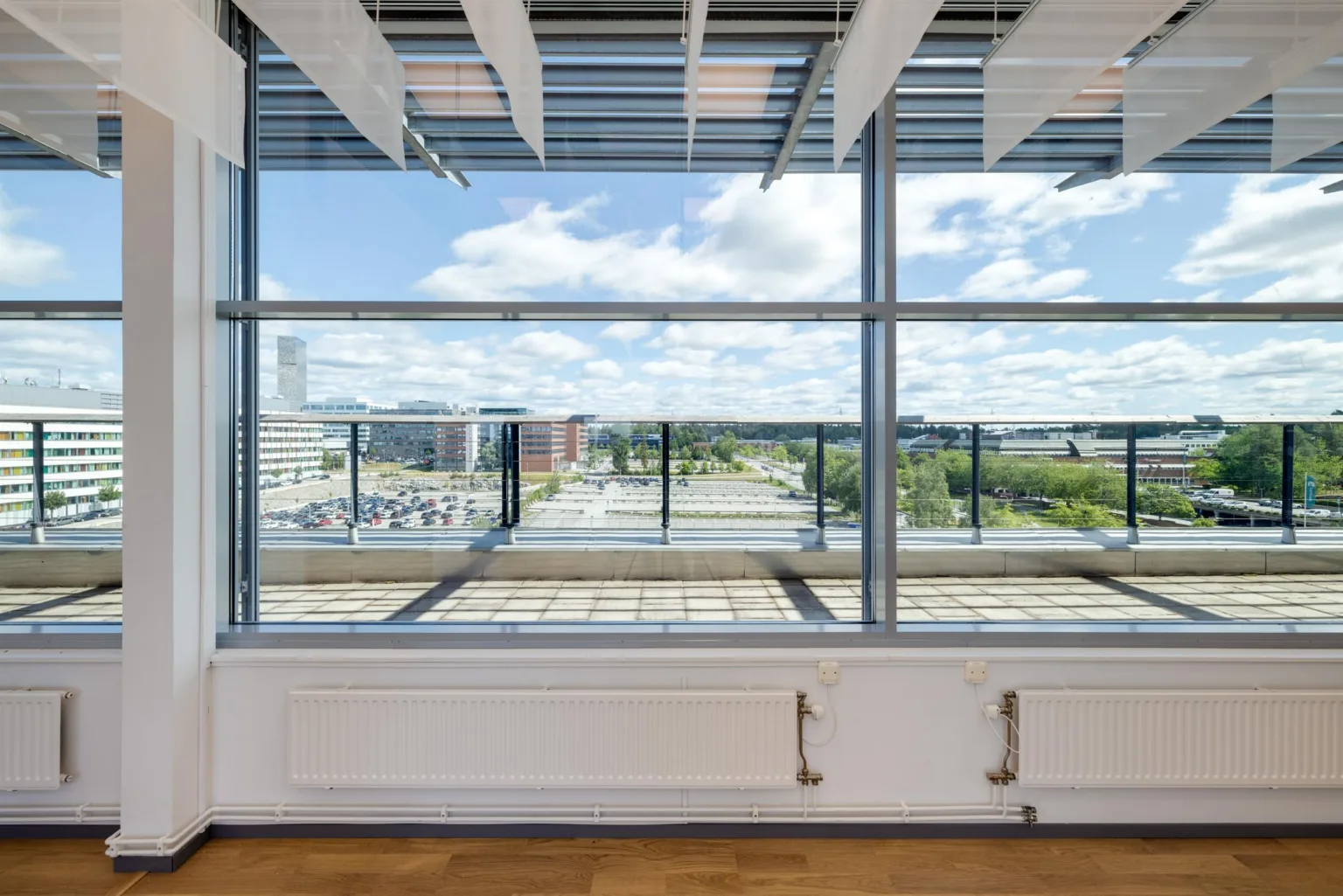 1. Stora fönster med utsikt över en grön park och moderna byggnader, ljusinsläpp från molnig himmel.