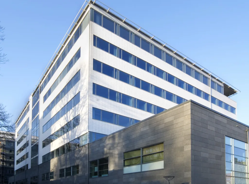 En vit kontorsbyggnad med glasfönster och en grå betongbas, belyst av dagsljus.