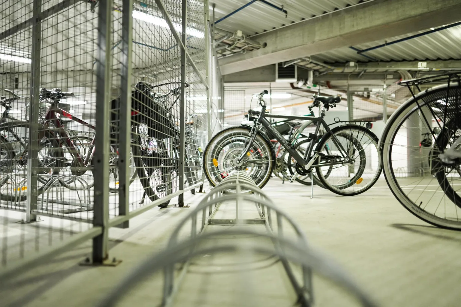 En cykelparkering inomhus med flera cyklar och ett metallstaket.