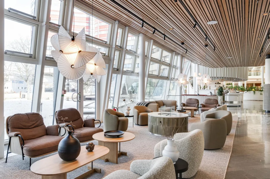 En lounge med bekväma fåtöljer, träbord, designlampor och stora glasväggar.