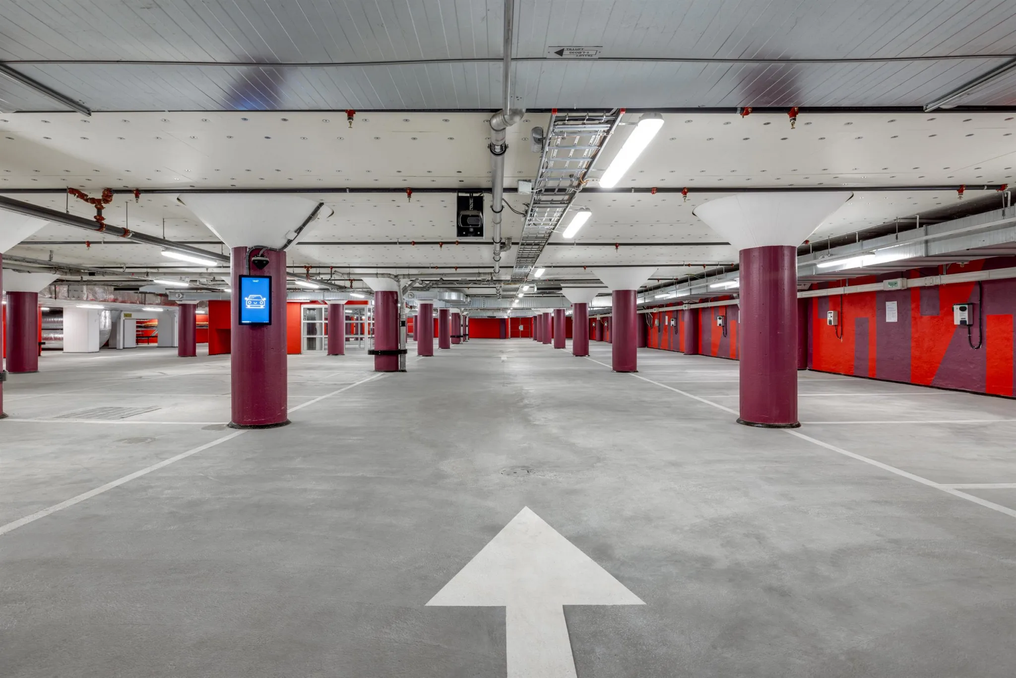 3. En tom parkeringsplats inomhus med röda pelare och en vit pil på golvet.