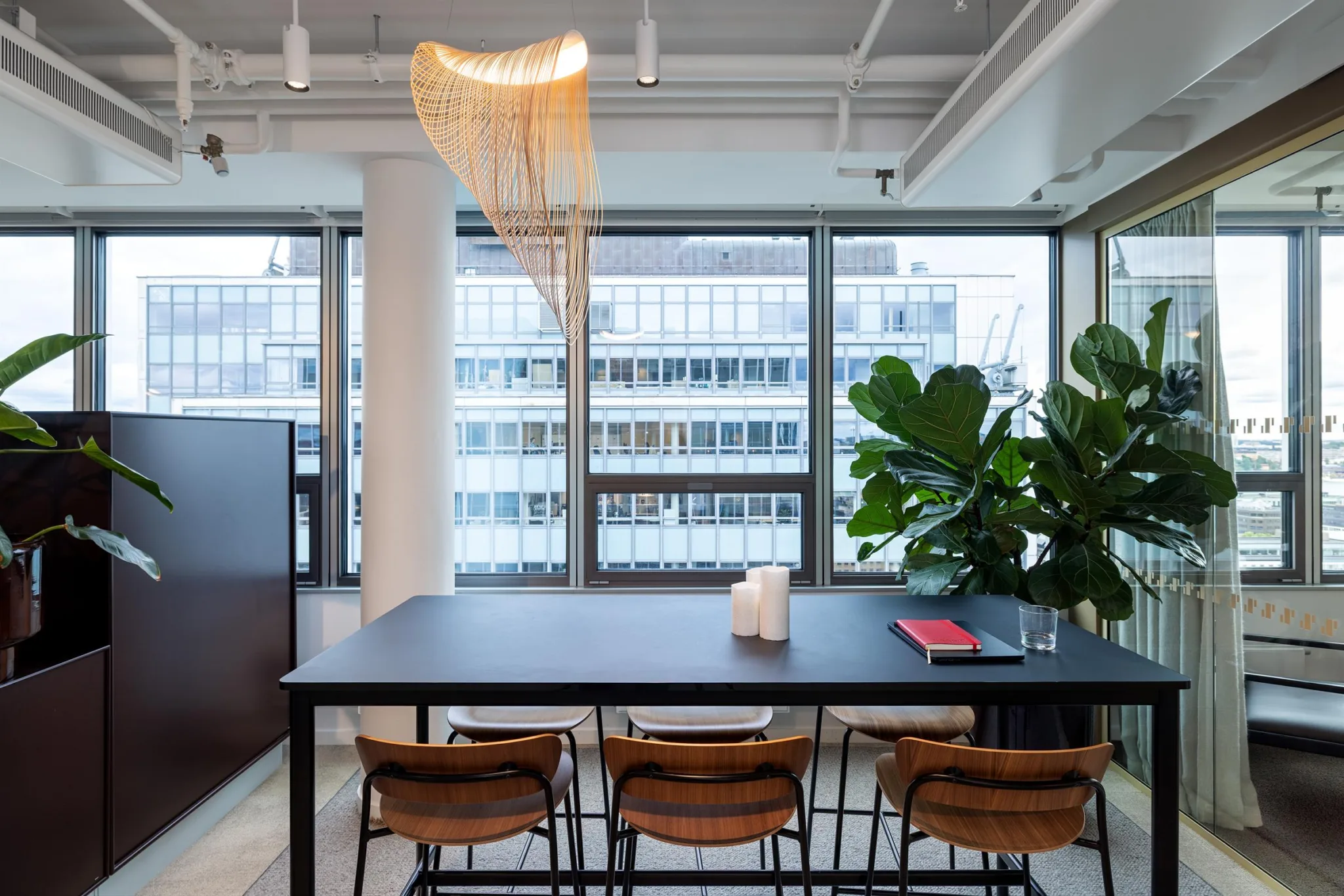 1. Ett modernt kontorsutrymme med ett bord, fyra stolar, stora fönster och en hängande designlampa.