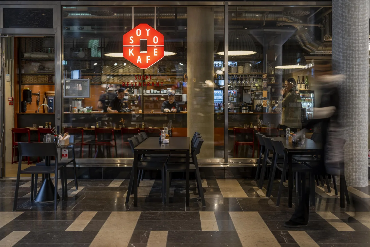 5. Ett café med svarta bord och stolar, en röd ljusskylt med texten "Soto Kafé" och en synlig bardisk i bakgrunden.