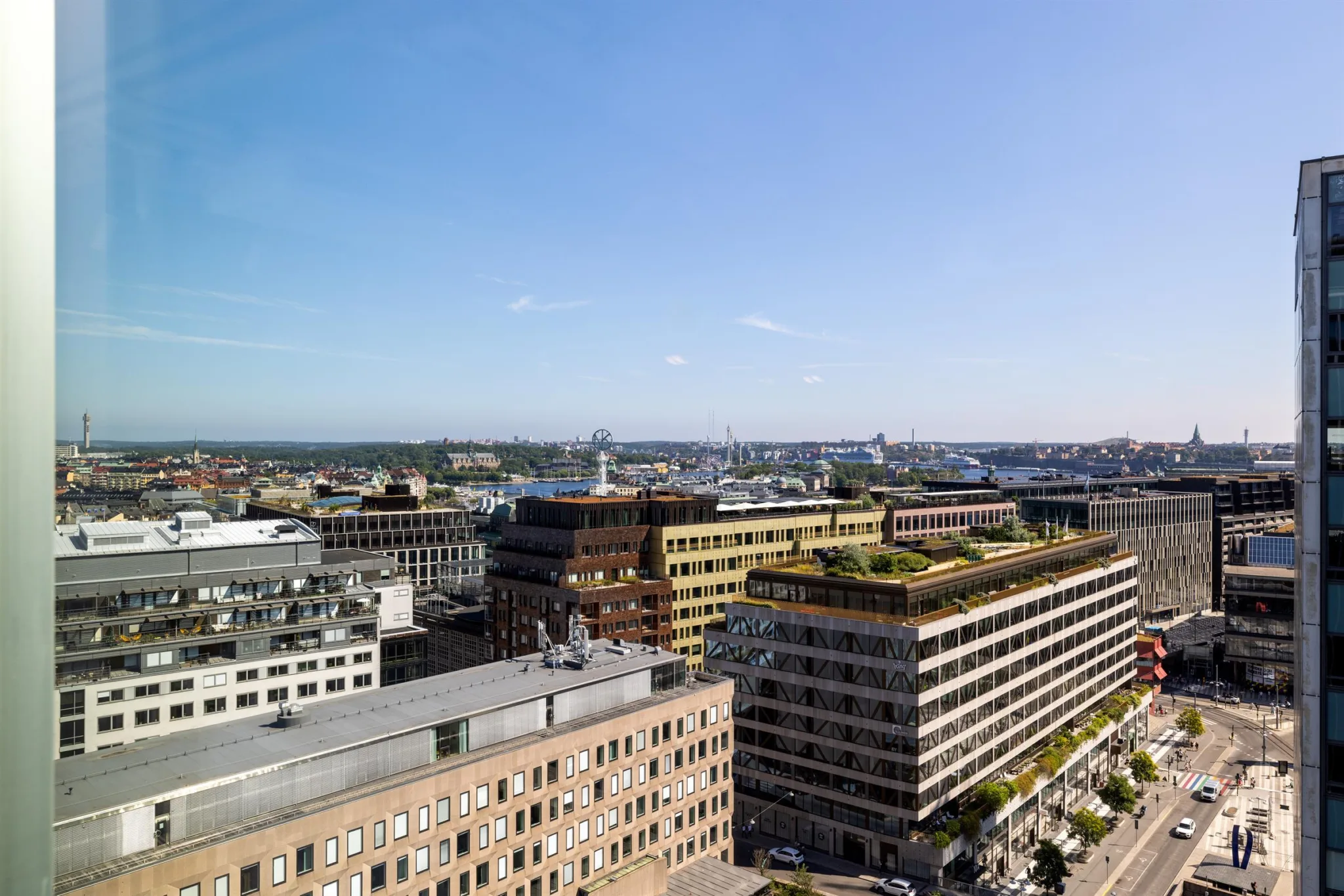 1. Stadsvy med flera byggnader, varav en har ett grönt tak, under en klarblå himmel.